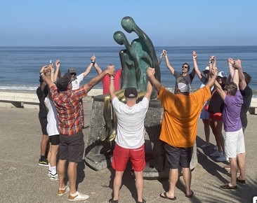 Equipo corporativo tomado de las manos alrededor de una escultura en el Malecón de Puerto Vallarta durante una actividad de team building